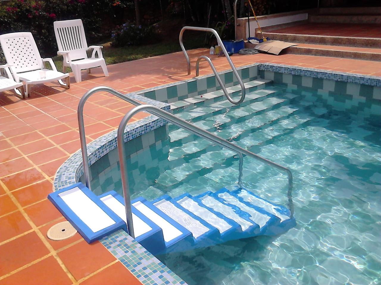 Escalera de acceso en fibra de vidrio con pasamanos en acero inoxidable, instalada por ArquiPiscinas para el ingreso seguro de personas de la tercera edad a la piscina