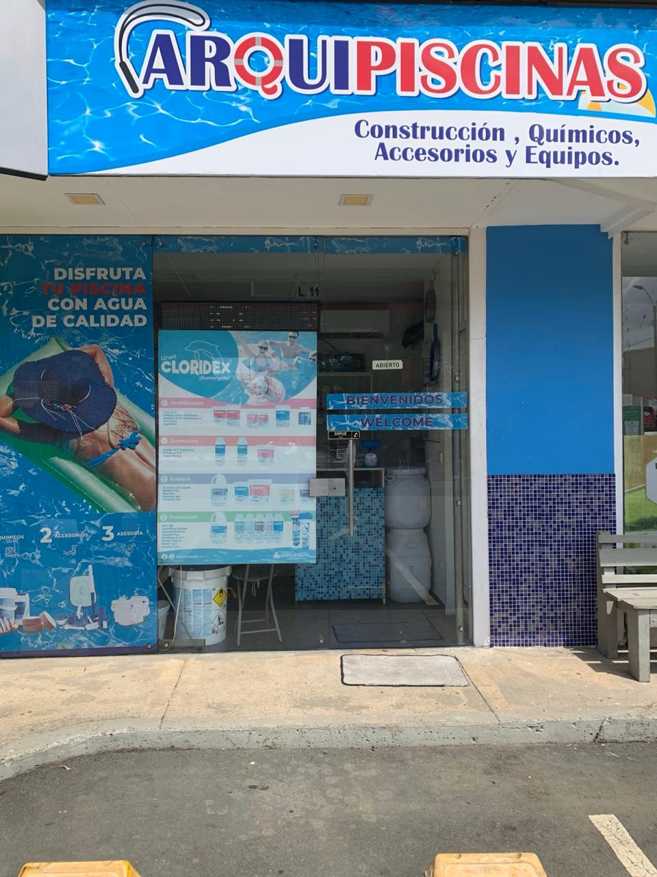 Entrada del local de ArquiPiscinas: aviso ARQUIPISCINAS, vitrinas con productos y letrero de bienvenida en la puerta