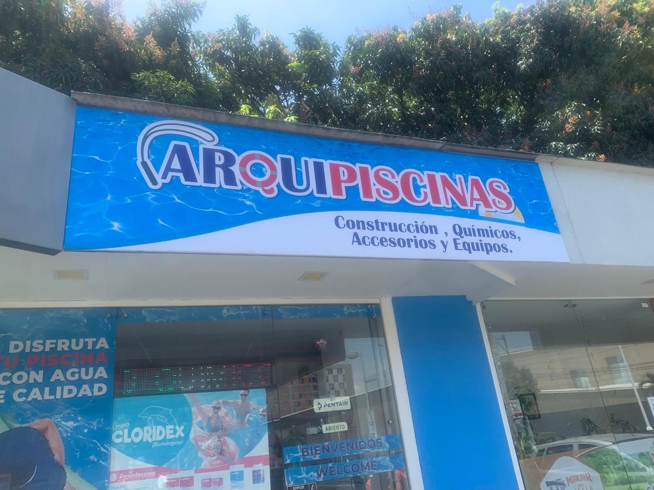 Fachada completa del local de ArquiPiscinas, con el aviso ARQUIPISCINAS sobre fondo de cielo azul
